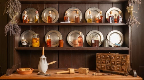 Wooden pantry shelves at Quebec house lined with pewter plates, bottles and containers of preserved ingredients, spice drawer and cooking implements on the work surface and lavender bunches drying on the sides